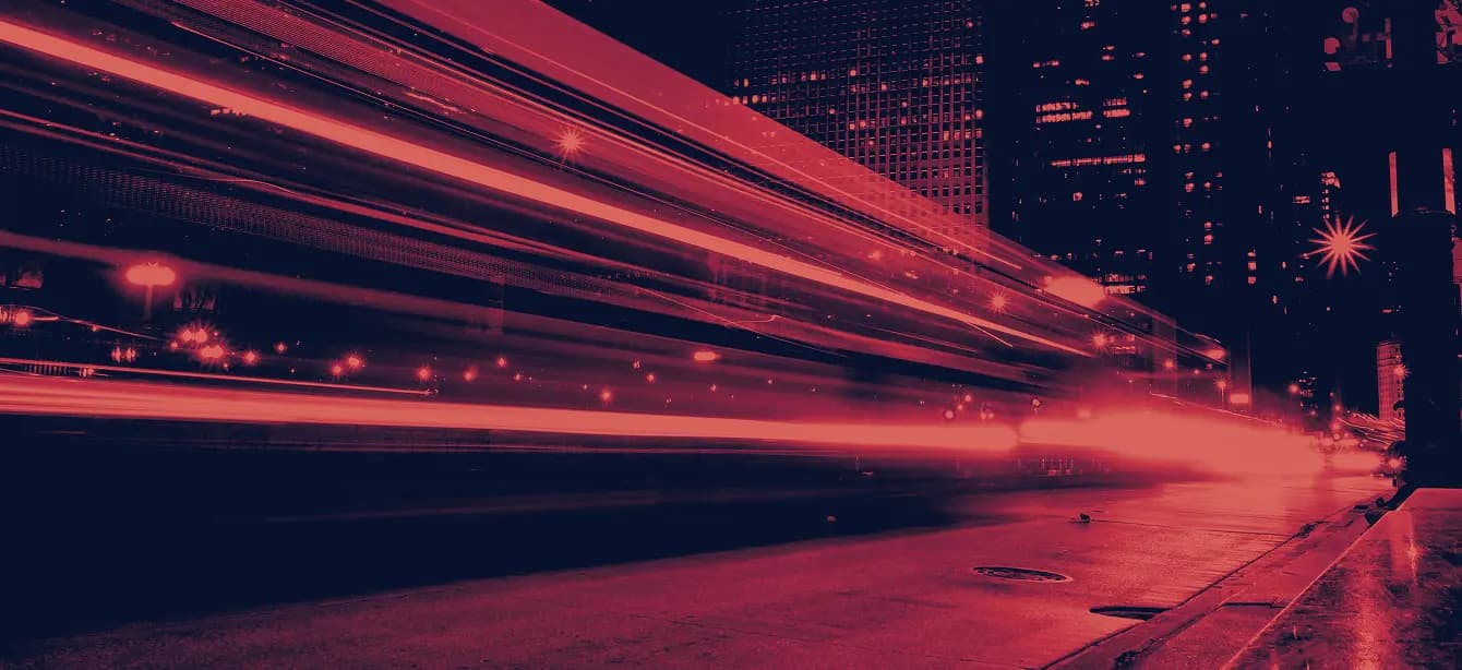 Night city street with red light trails from fast-moving traffic among tall buildings.