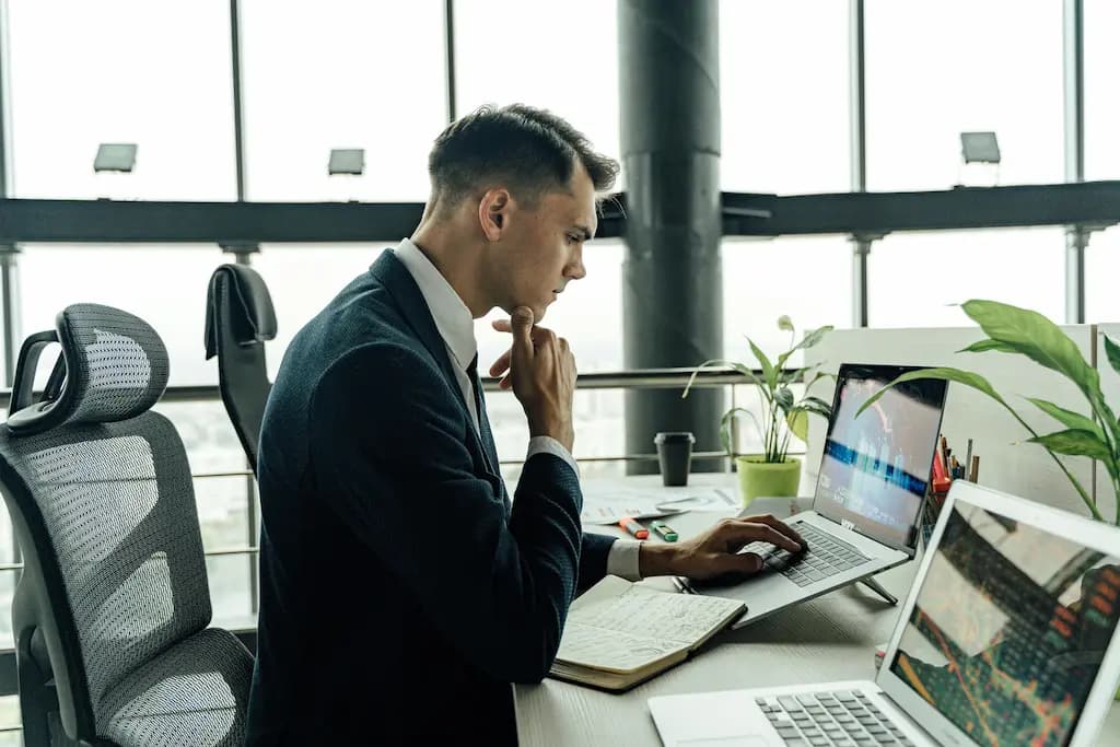 Man in a suit analyzing financial charts on a laptop at a modern office desk with plants.
