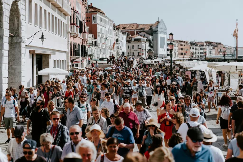 Crowded street filled with tourists walking among market stalls in a historic European city.