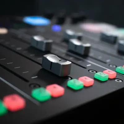 Close-up of an audio mixing console with sliders and illuminated buttons.